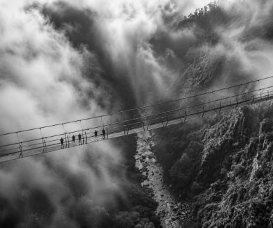 Imagem a preto e branco da Ponte 516 Arouca a atravessar o vale do rio Paiva entre neblina densa e encostas rochosas, com vários visitantes agrupados numa secção da ponte suspensa.