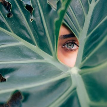 woman-peeking-over-green-leaf-plant-taken-at-daytime-cTKGZJTMJQU