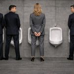 quatro profissionais de fato junto a urinóis numa casa de banho pública, com uma mulher ao centro