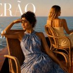 Duas mulheres elegantes sentadas num barco ao pôr do sol, usando vestidos fluidos de verão, inspiradas nas tendências de moda do Verão 2026.