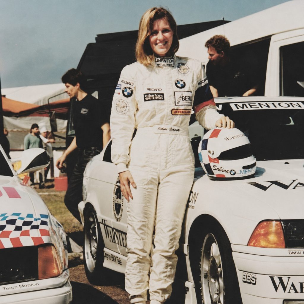 Sabine Schmitz em macacão de corrida ao lado de um carro de corrida na década de 1990
